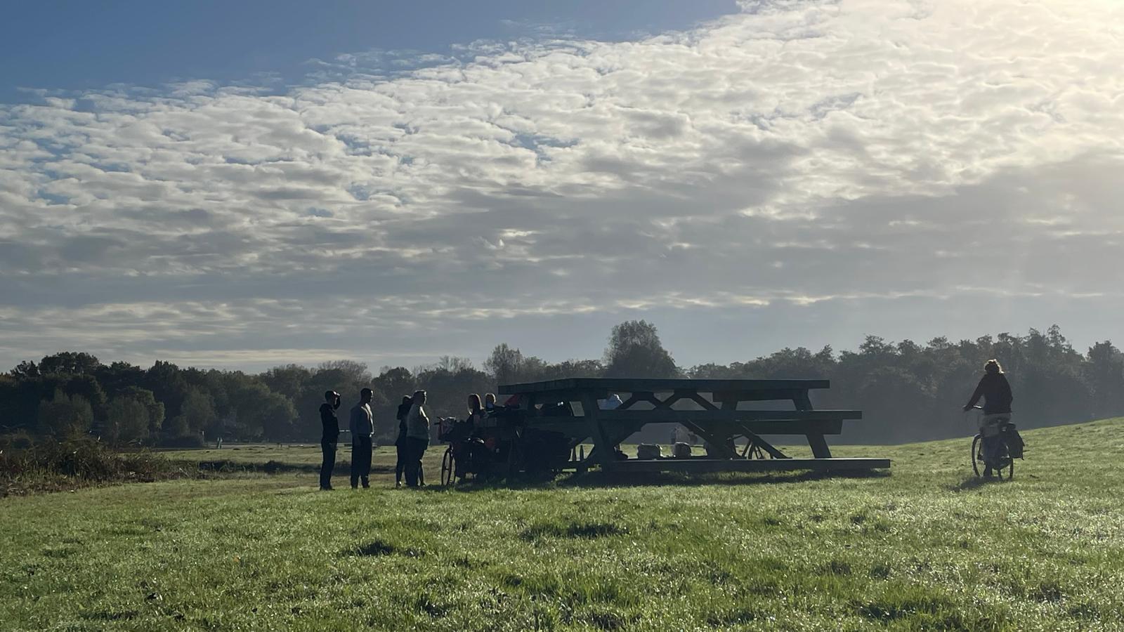 Groep mensen bijeen rond een grote houten picknicktafel in de wei